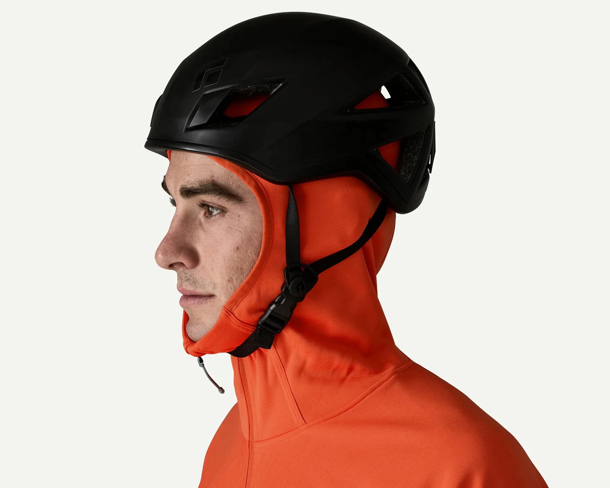 Side view of a person wearing a black helmet and an orange hooded jacket with the hood up.