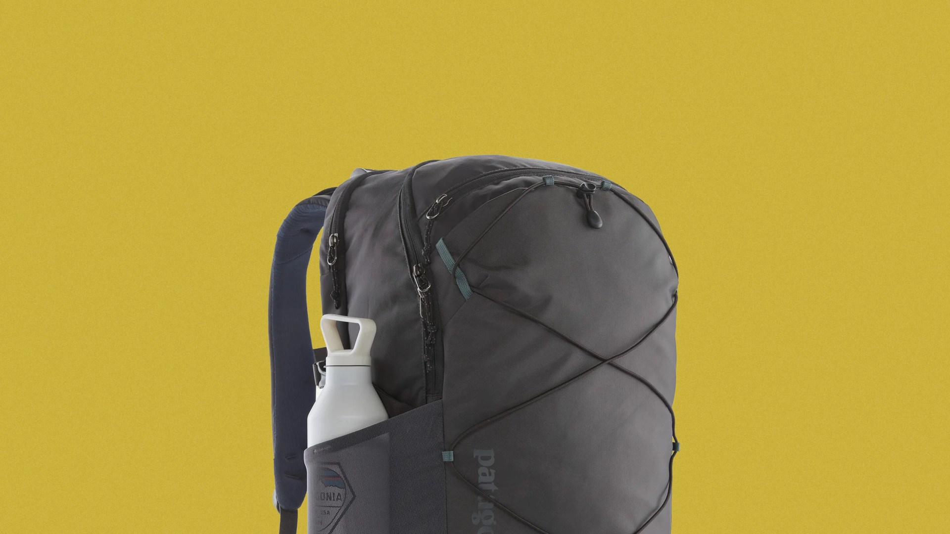 Dark gray Patagonia backpack with black bungee cords and a white water bottle in the side pocket against a yellow background.