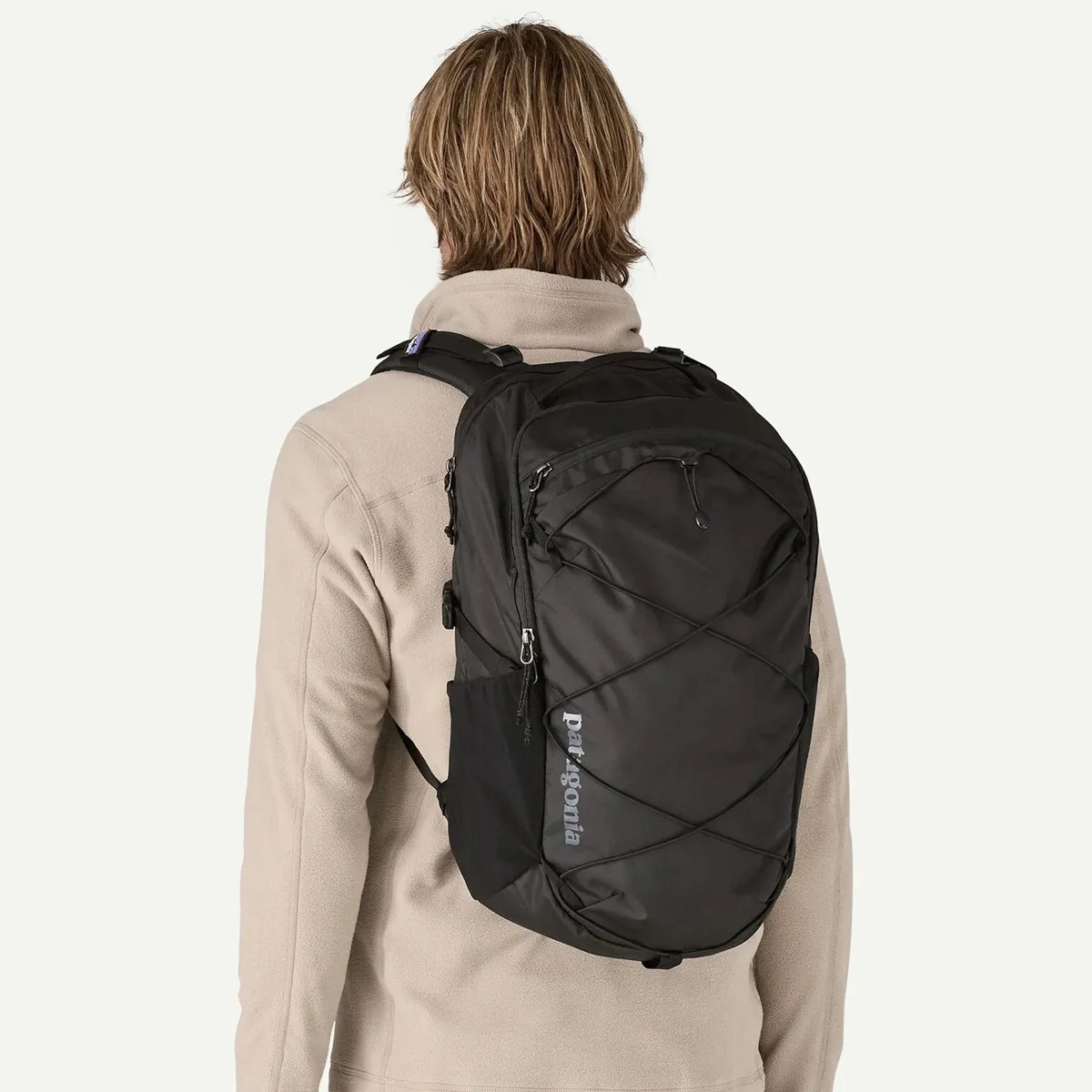 Black Patagonia backpack with front bungee cords worn by a person in a beige fleece jacket.