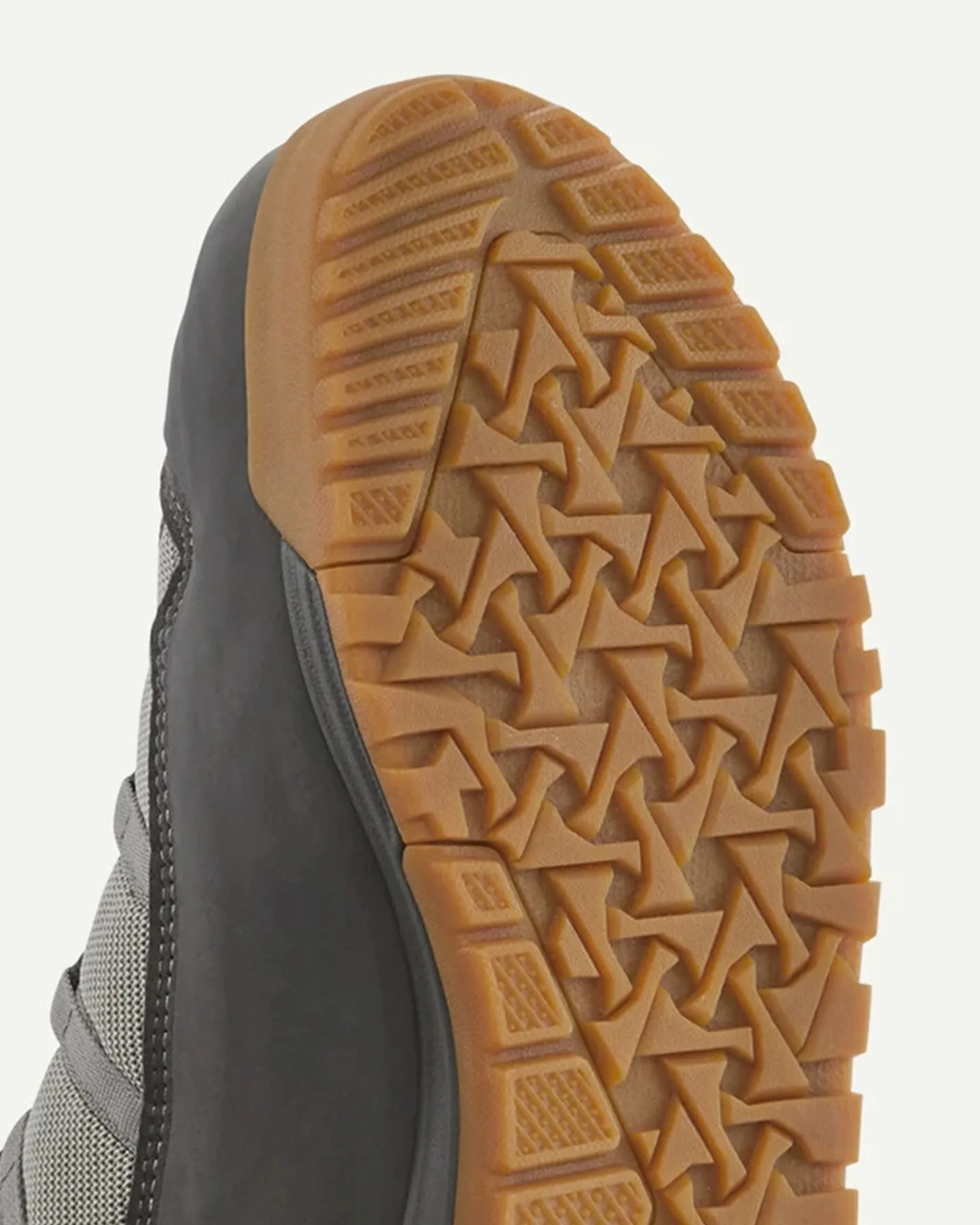 Close-up of a shoe sole with a tan rubber tread featuring a geometric pattern and a gray upper side.