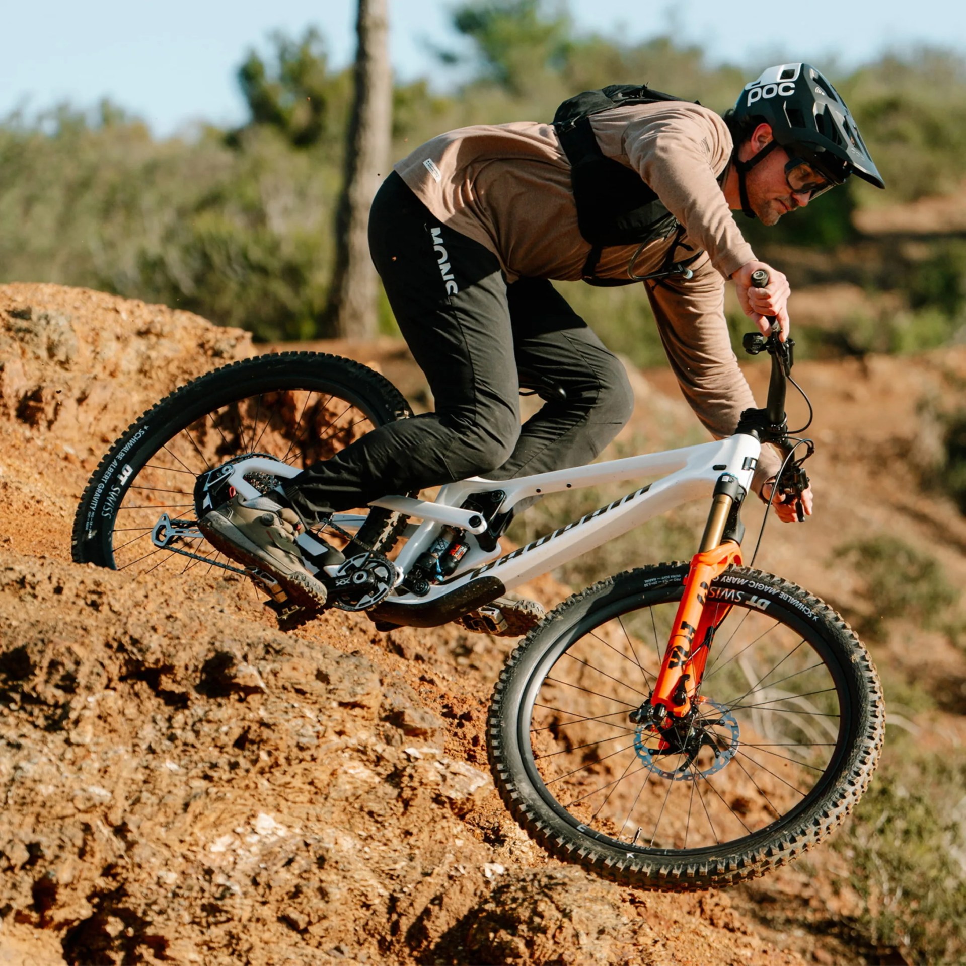 Person wearing a black helmet and brown jacket riding a white mountain bike with orange front suspension on a dirt trail.