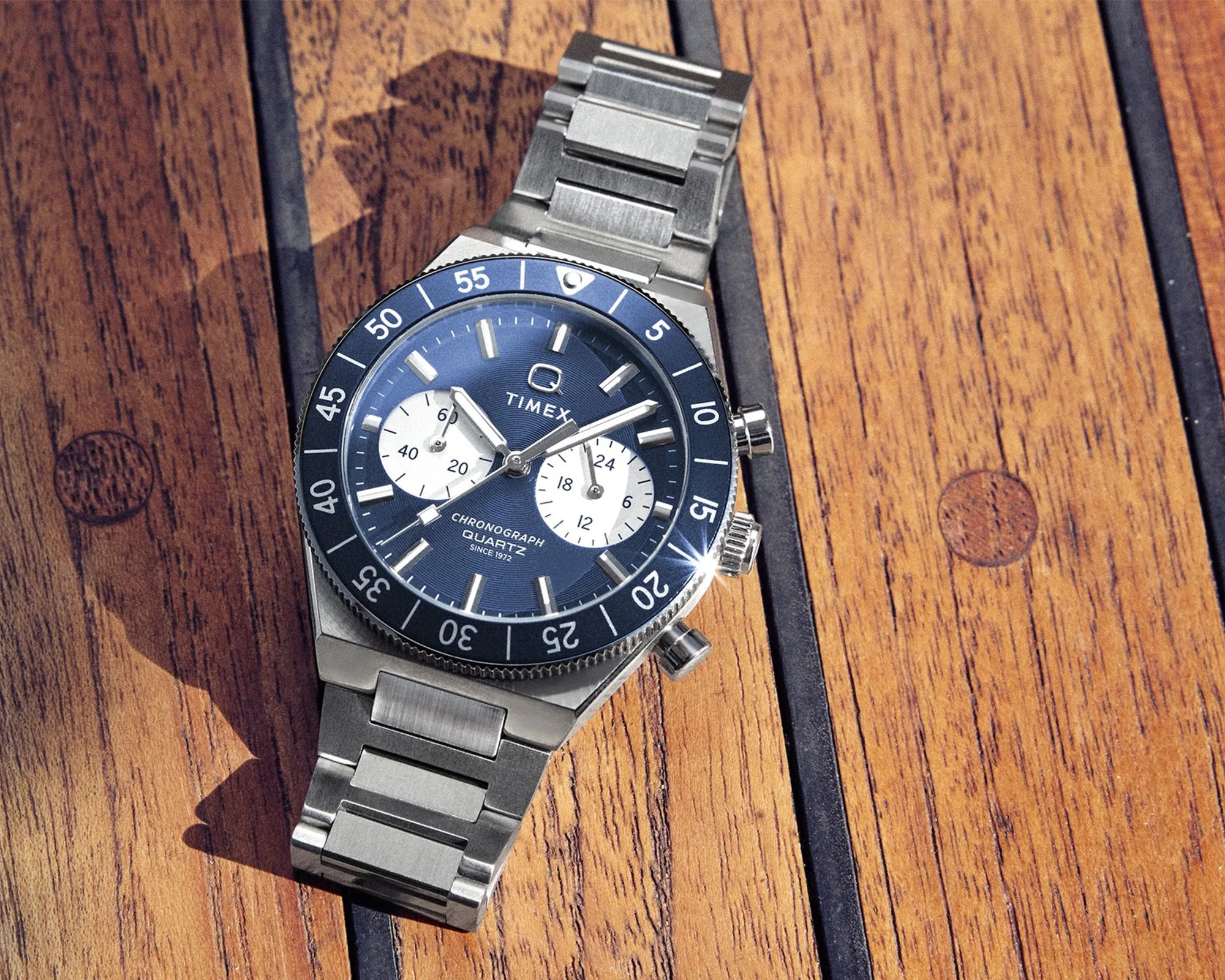 Silver Timex chronograph wristwatch with blue dial and bezel on a wooden surface.