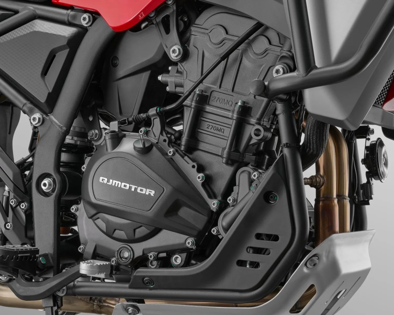 Close-up of a black QJMotor motorcycle engine with visible frame, exhaust pipes, and protective skid plate.