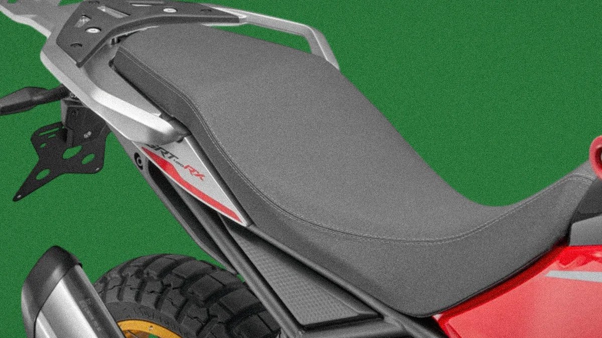 Close-up of a gray motorcycle seat with a silver rear rack and part of a rear tire and exhaust visible.