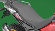 Close-up of a gray motorcycle seat with a silver rear rack and part of a rear tire and exhaust visible.