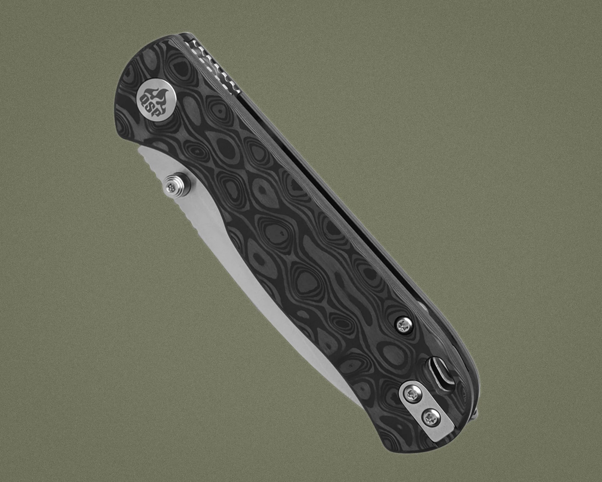 Black and gray patterned folding knife with partially serrated blade and metal clip on olive background.
