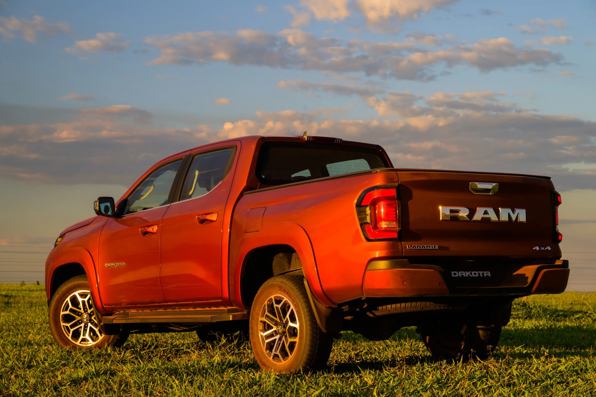 Orange RAM Dakota Laramie 4x4 pickup truck parked on grass under a partly cloudy sky at sunset.