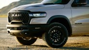 Front side view of a silver RAM truck with black grille and off-road Goodyear Wrangler tires on dry ground.