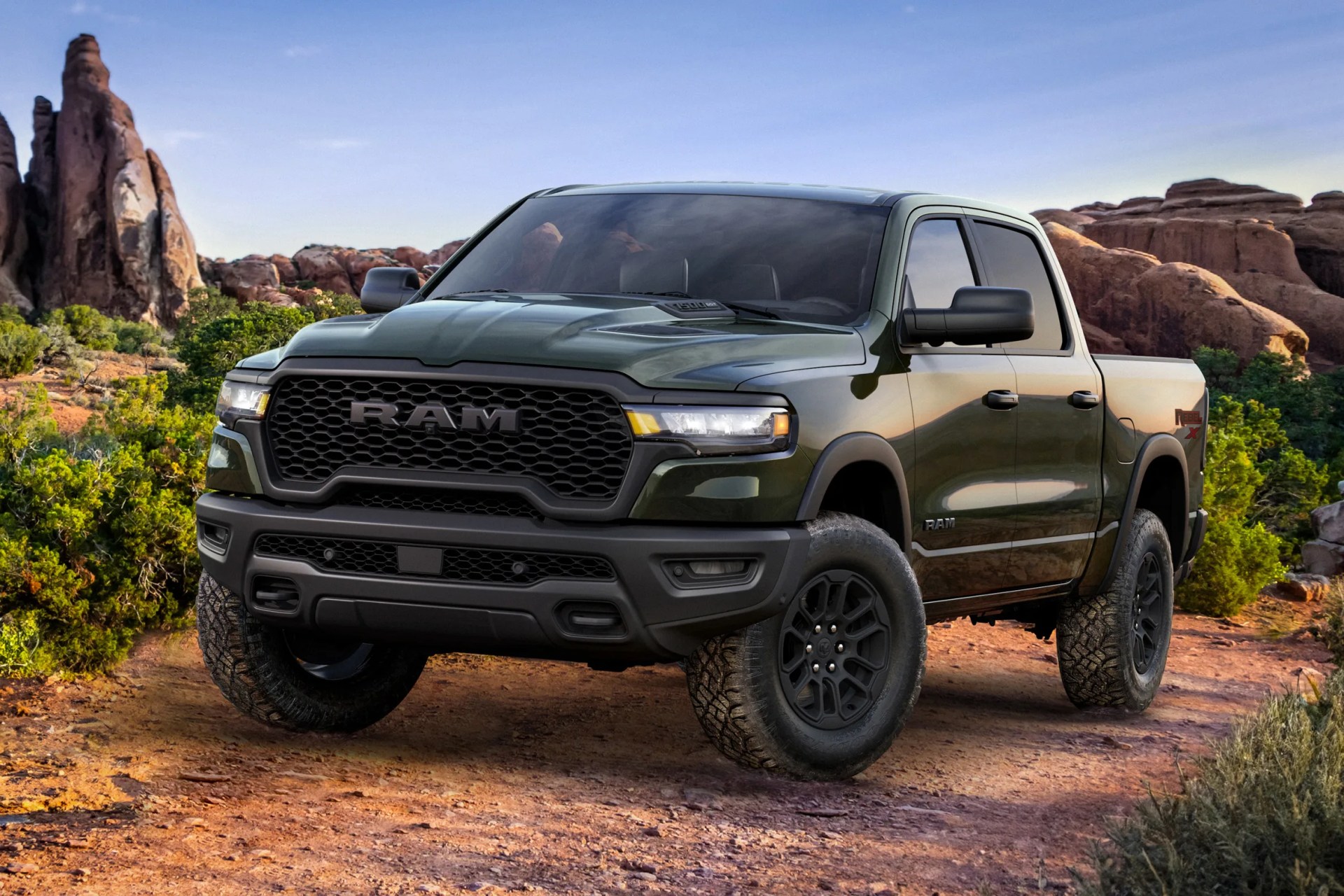 Dark green RAM pickup truck with black grille and off-road tires parked on a dirt trail in a rocky desert landscape.