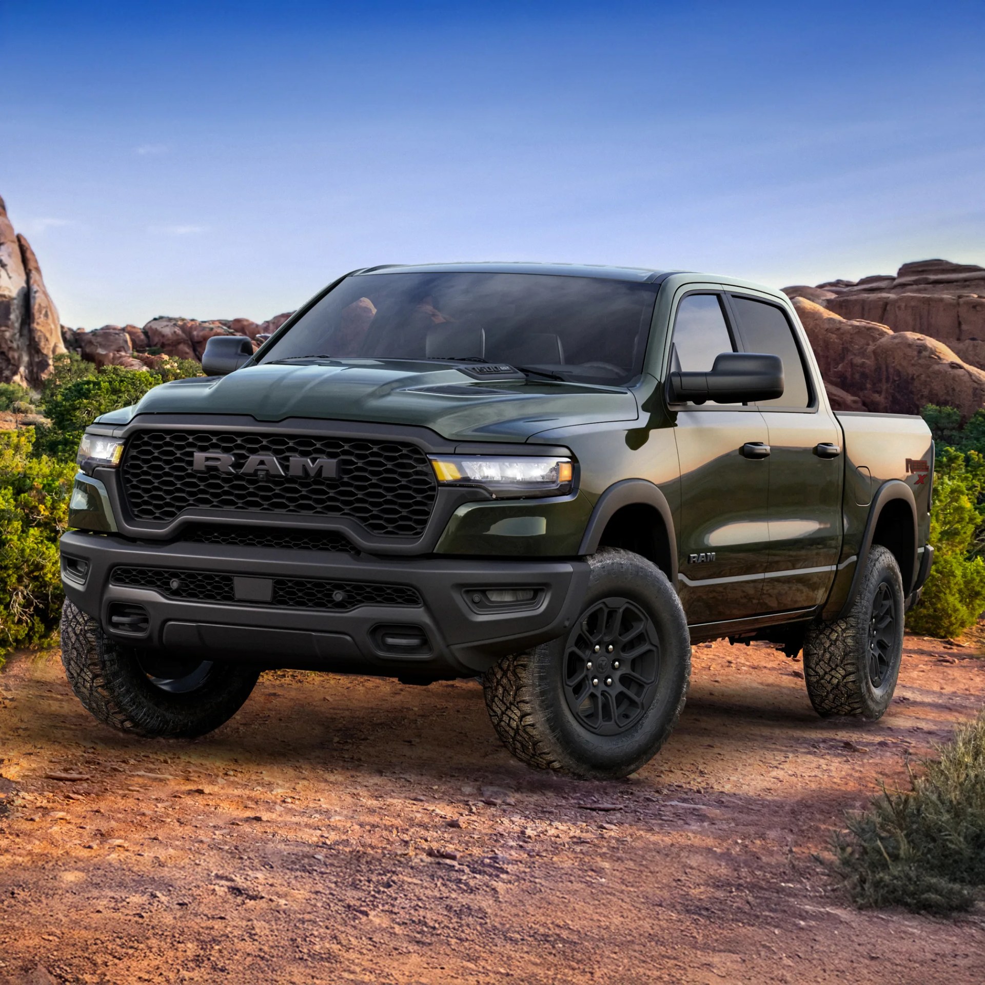 Dark green RAM pickup truck with black grille and off-road tires parked on a dirt trail in a rocky desert landscape.