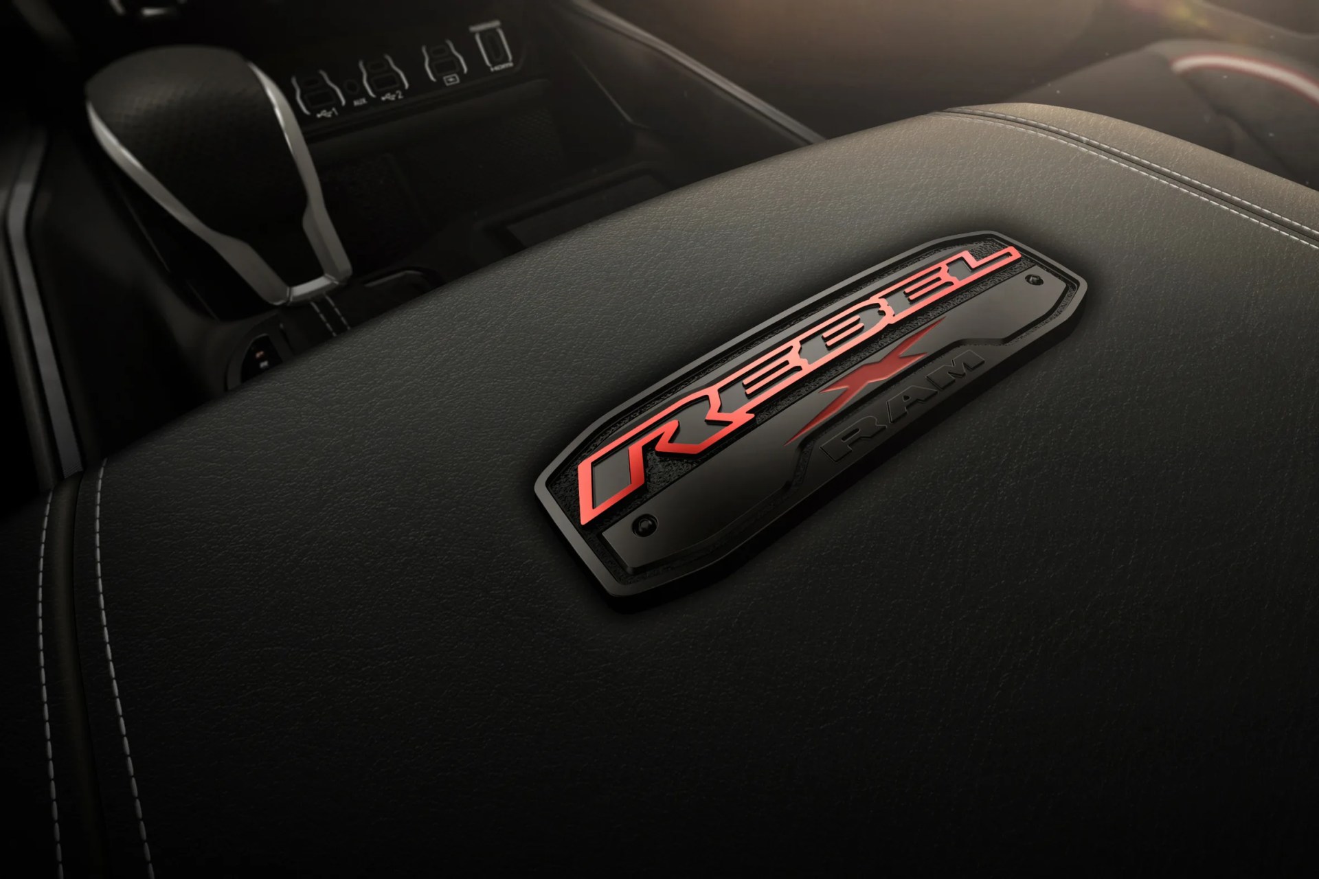 Black leather car armrest with red "Rebel X RAM" emblem and white stitching near a gear shift.