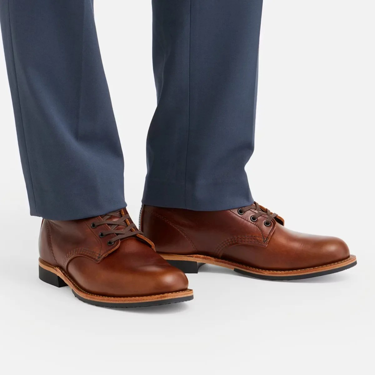 Pair of brown leather lace-up boots worn with navy blue pants on a white background.
