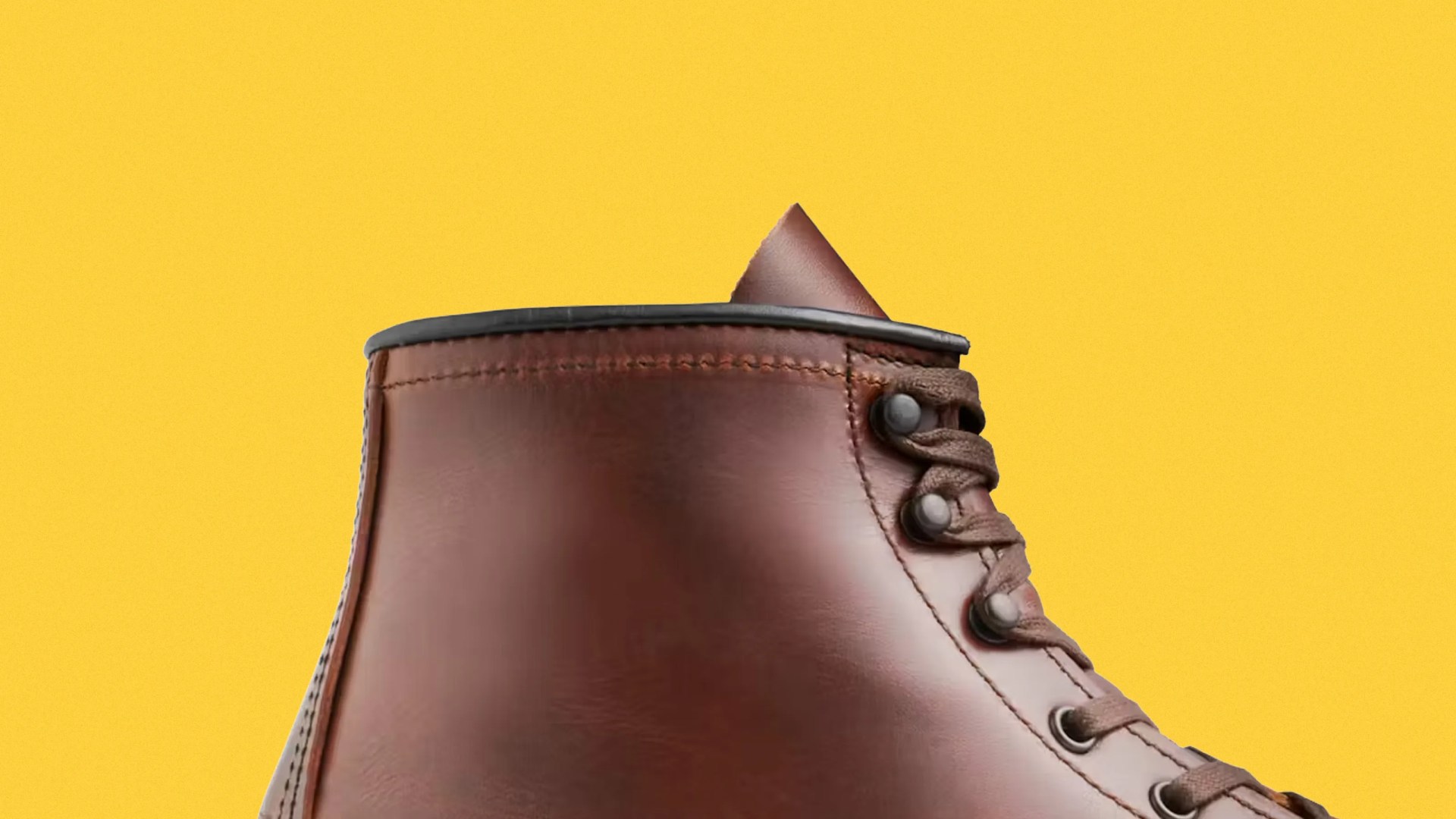 Close-up of the upper part of a brown leather boot with laces against a yellow background.