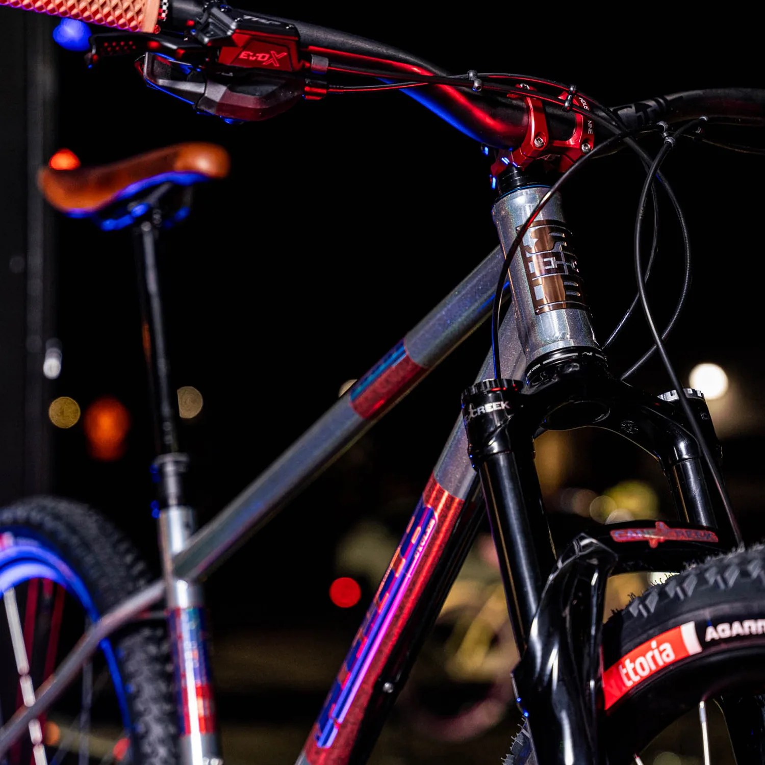Mountain bike with metallic gray frame, brown saddle, black suspension fork, and Vittoria tire at night.