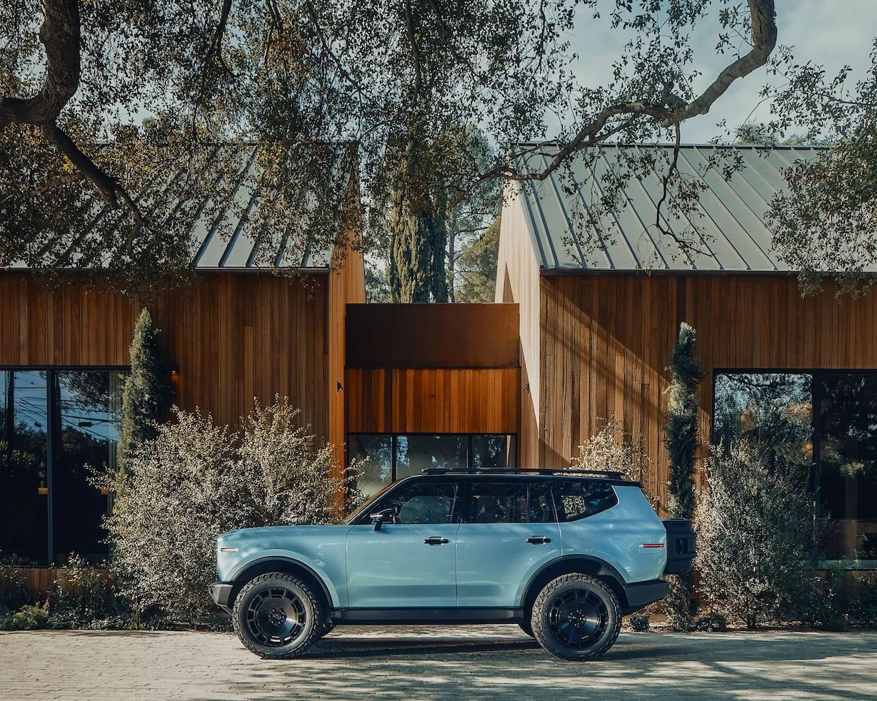 Light blue SUV with black roof and off-road tires parked in front of a modern wooden house with large windows.