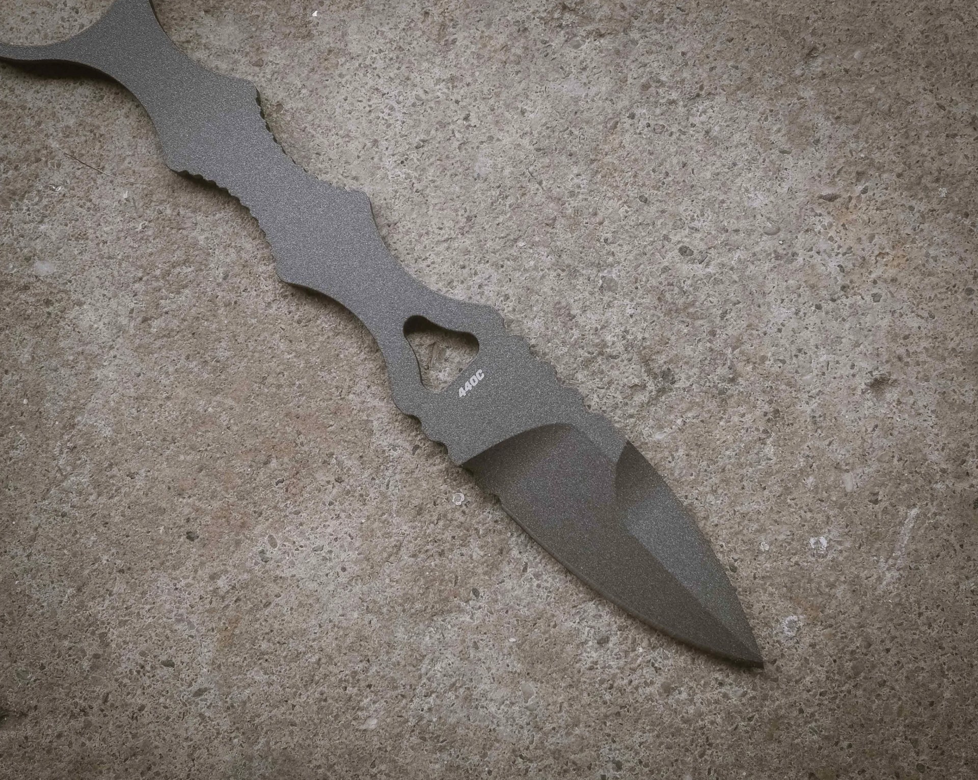 Gray tactical knife with a serrated handle and "440C" marking on a textured stone surface.