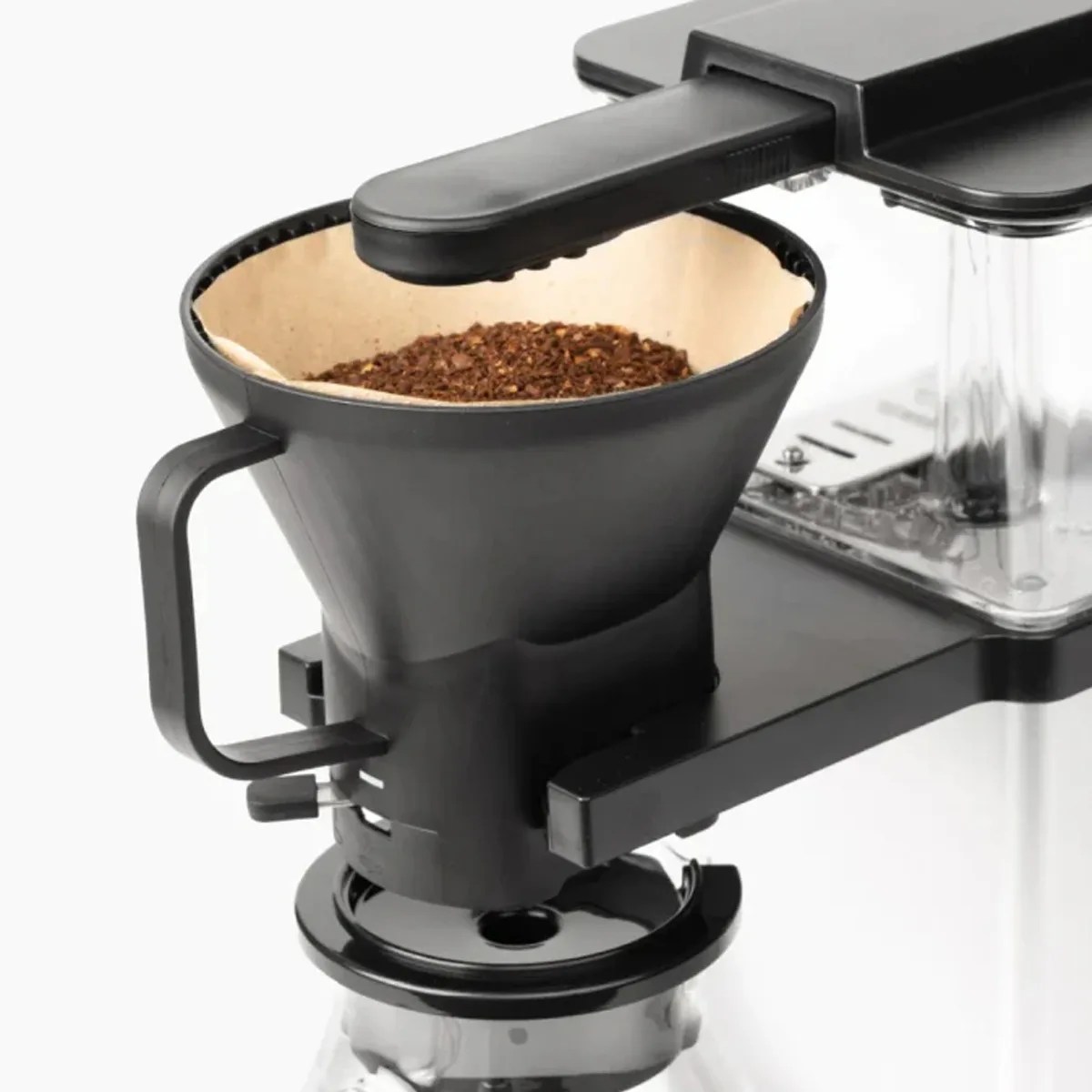 Black plastic coffee dripper with a paper filter and ground coffee inside, attached to a coffee maker.