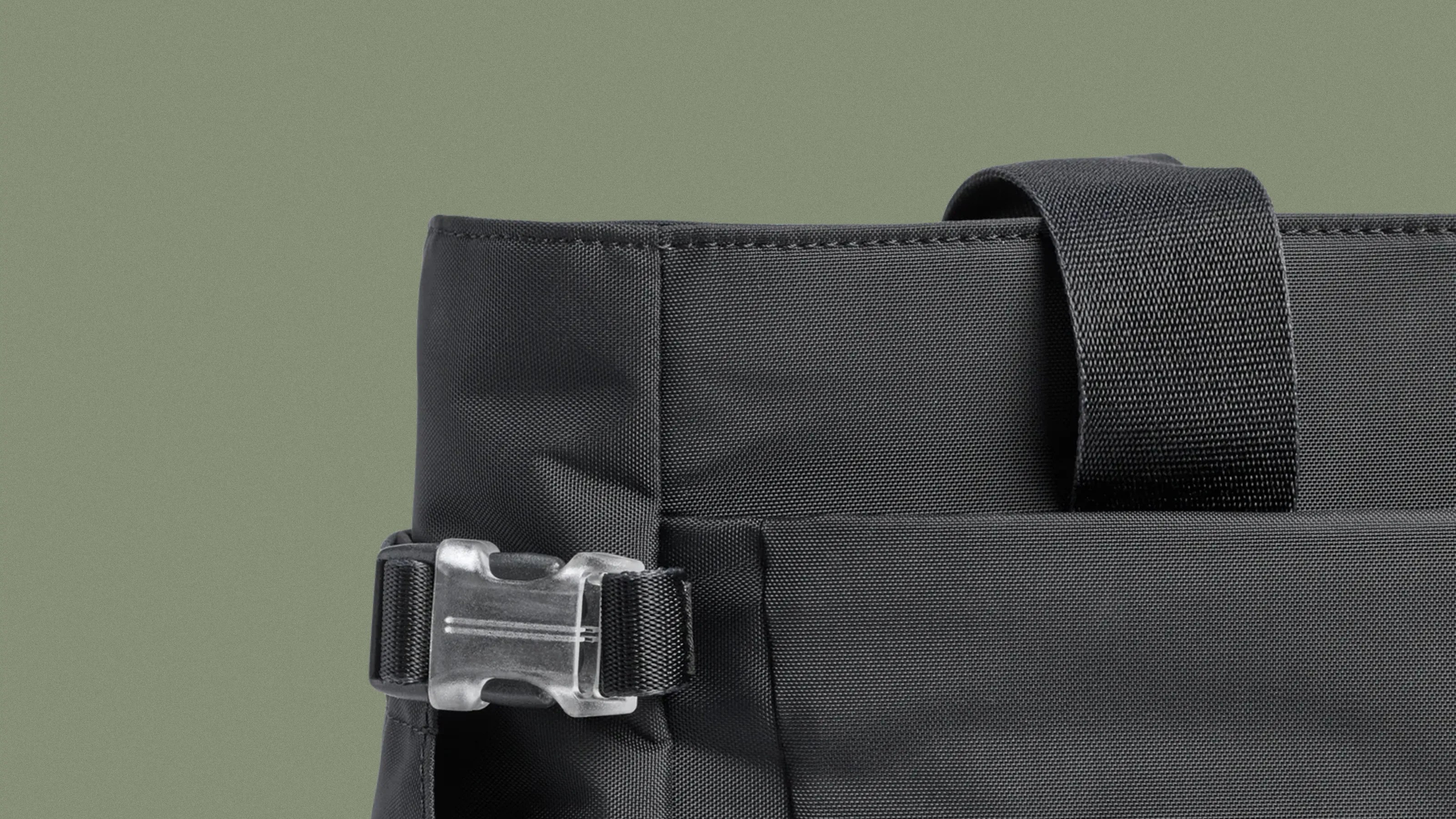 Close-up of a black fabric bag corner with a clear plastic buckle and a black strap loop.