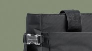 Close-up of a black fabric bag corner with a clear plastic buckle and a black strap loop.