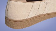 Close-up of beige suede Adidas sneaker with gum rubber sole and embossed Adidas logo on the side.