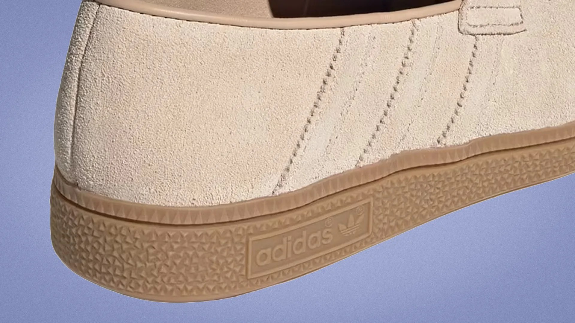Close-up of beige suede Adidas sneaker with gum rubber sole and embossed Adidas logo on the side.