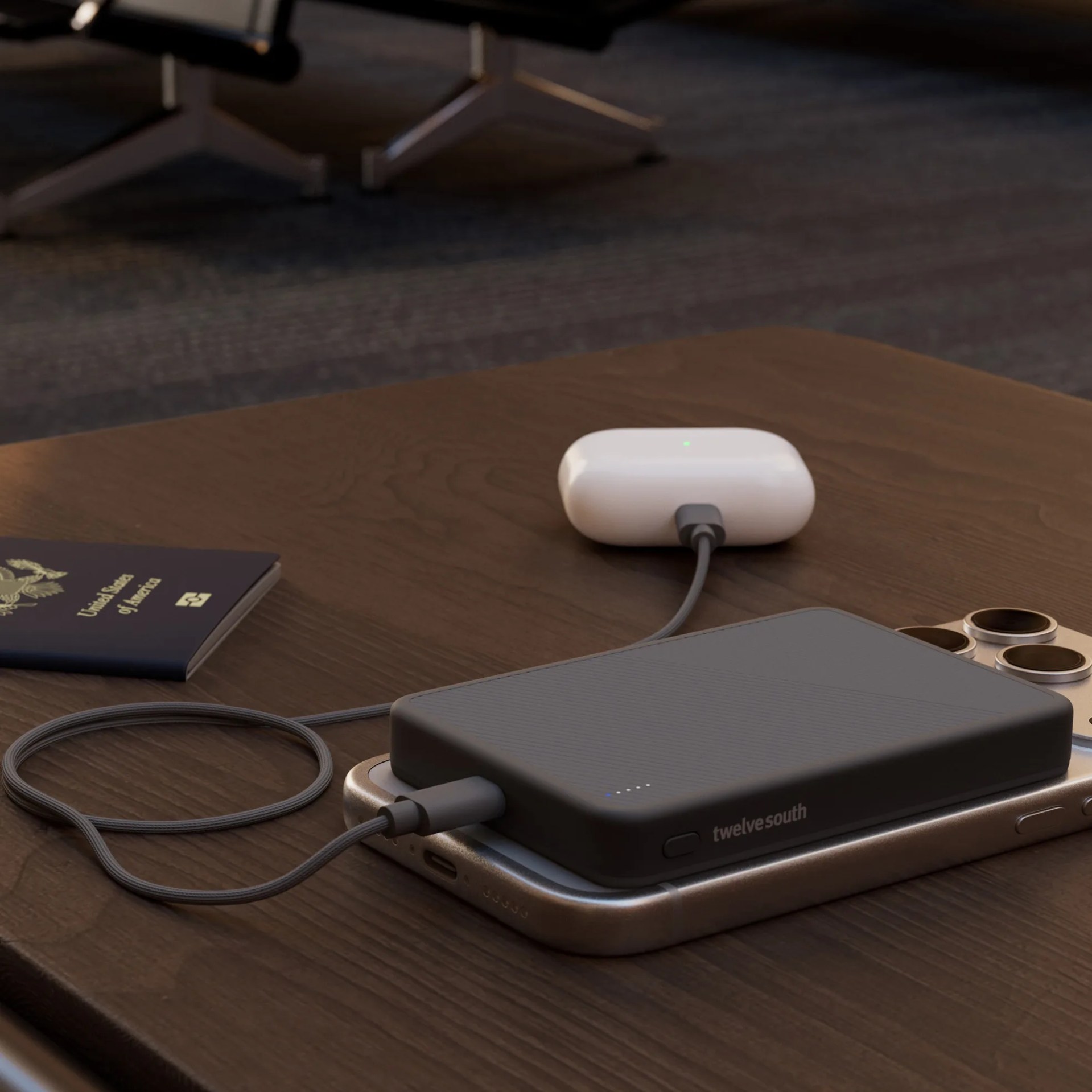 Black Twelve South portable charger connected to a silver smartphone and white wireless earbuds case on a wooden table.