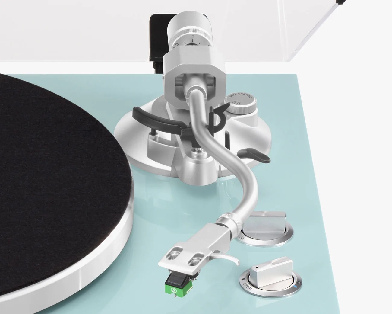 Close-up of a silver tonearm with a green cartridge on a light blue turntable with control knobs.