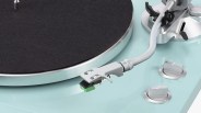 Close-up of a silver tonearm and black felt-covered platter on a light blue turntable.