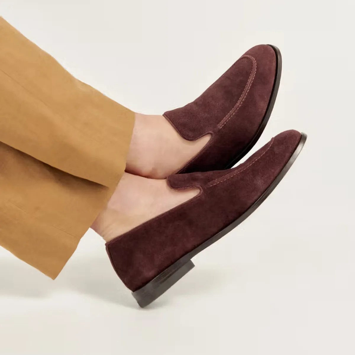 Pair of dark brown suede slip-on loafers worn with tan pants.