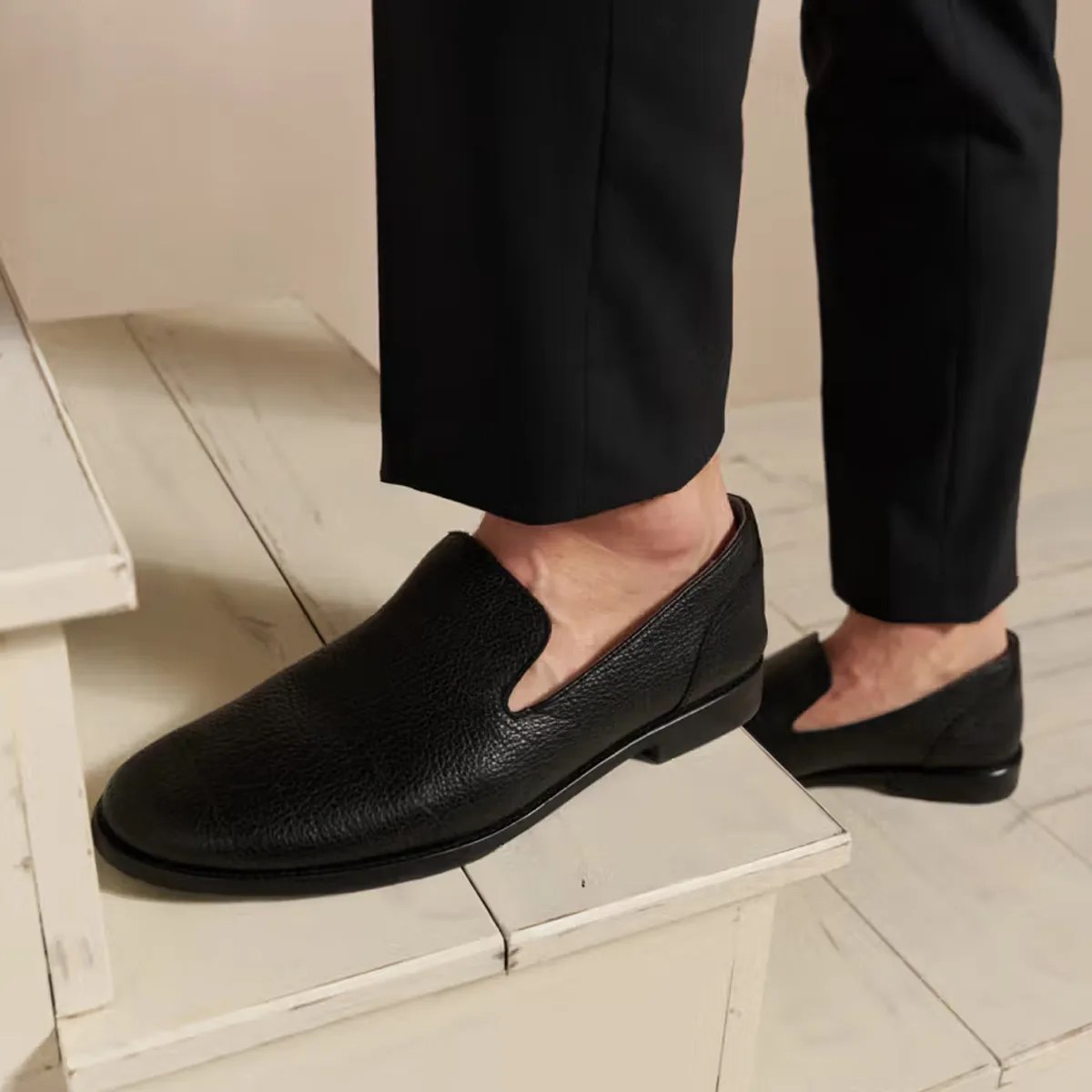 Pair of black textured leather slip-on dress shoes worn with black pants.