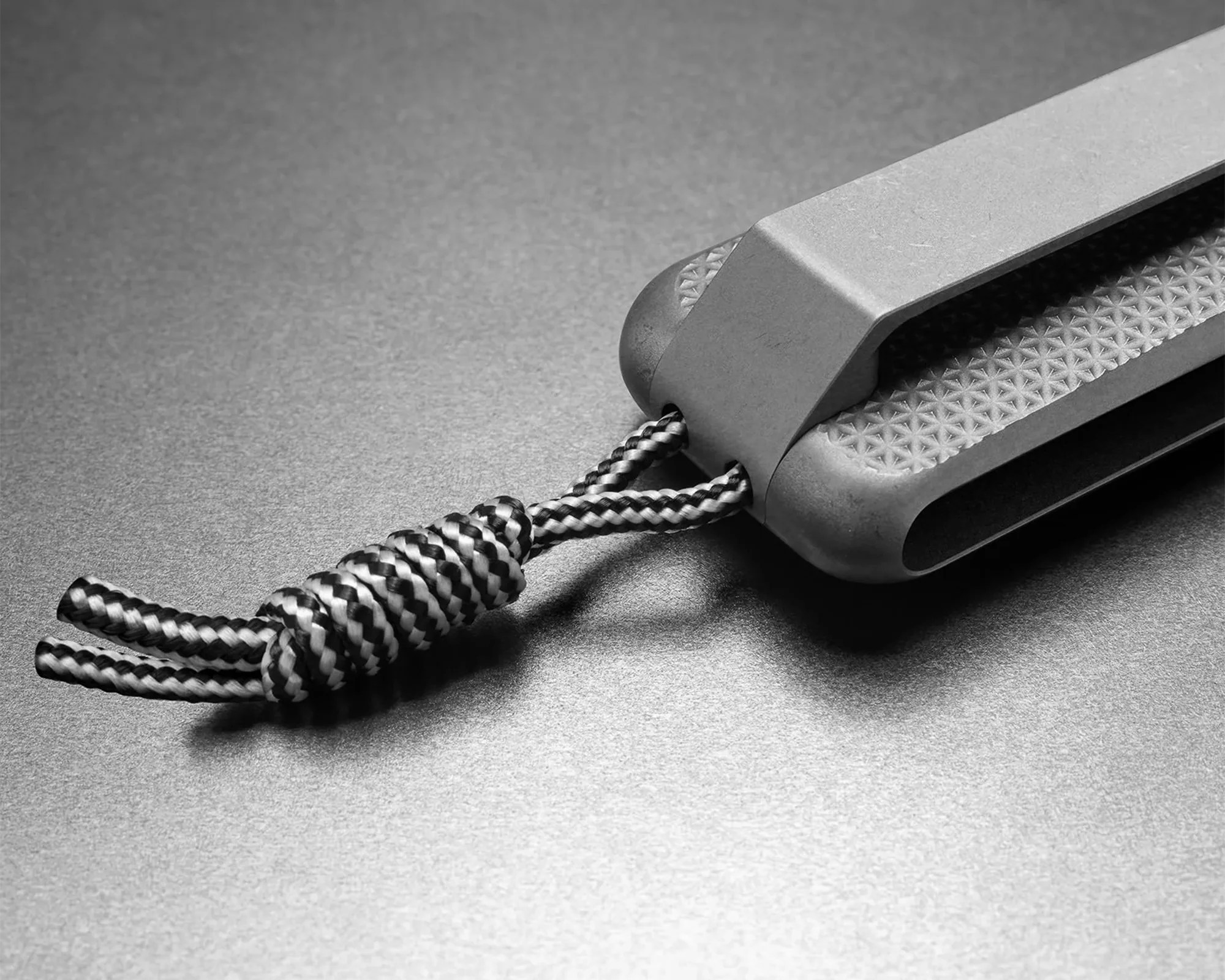 Close-up of a gray textured handle with a black and white braided cord looped through it on a metallic surface.