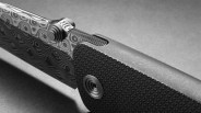 Close-up of a folding knife with a patterned Damascus steel blade and textured black handle.