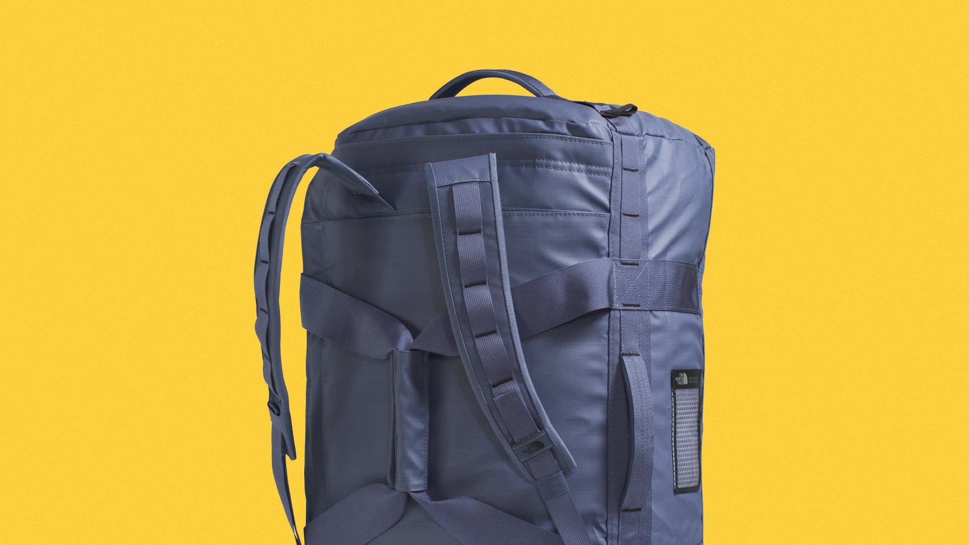 Blue North Face backpack with padded shoulder straps against a yellow background.