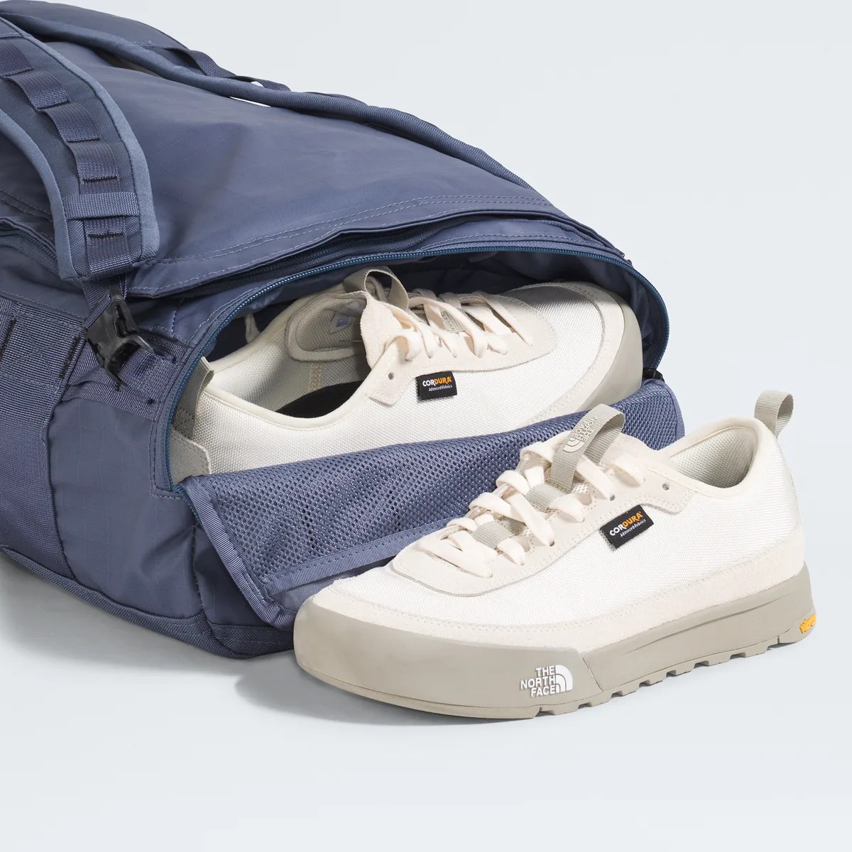 Pair of off-white The North Face sneakers with beige soles partially inside a blue duffel bag.