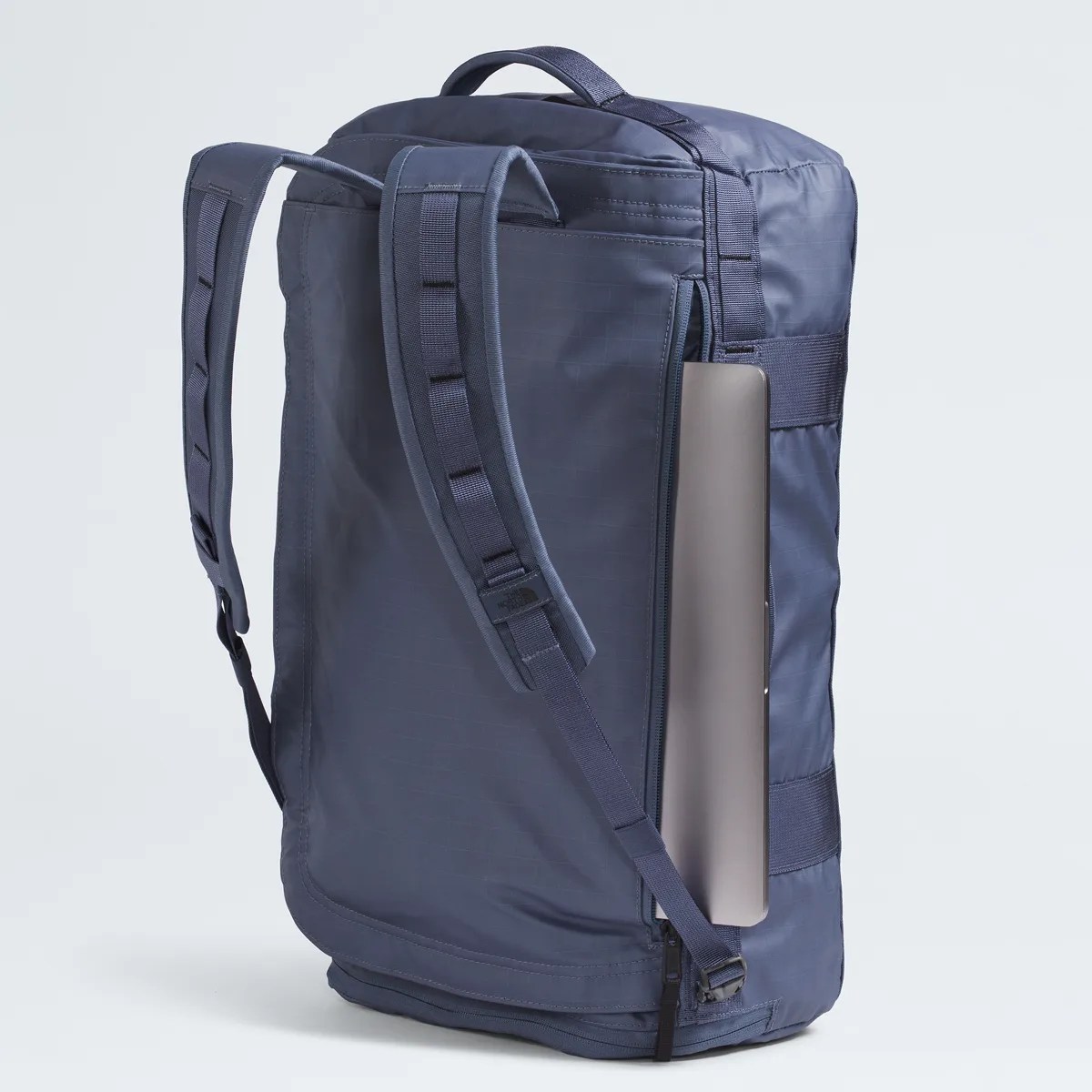 Navy blue backpack with padded shoulder straps and a laptop partially inserted in a side zipper pocket.