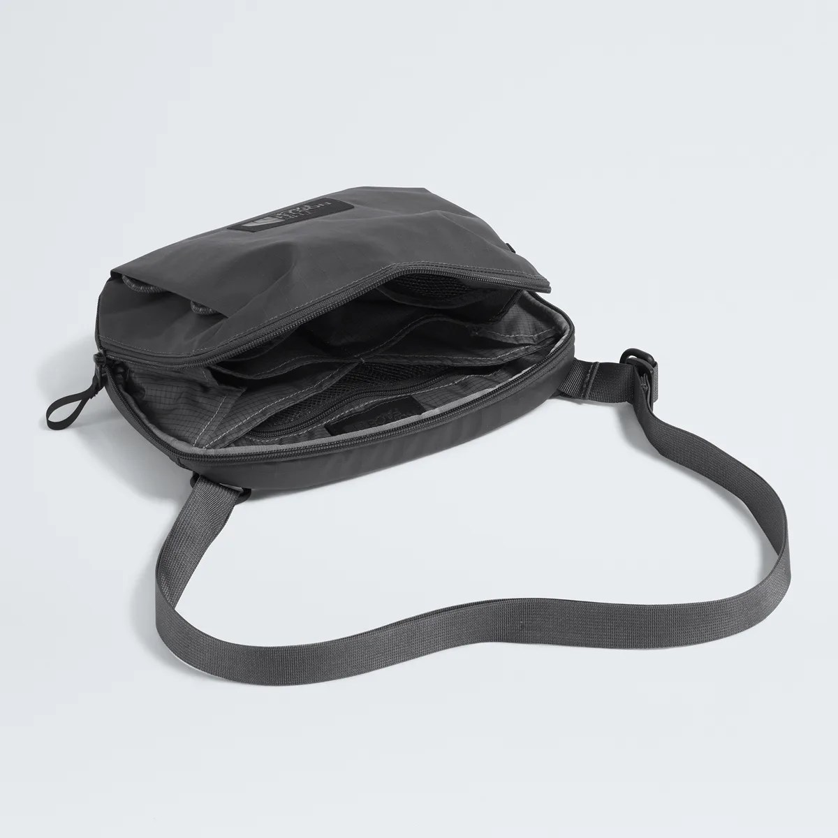 Black crossbody bag with adjustable strap and multiple interior compartments shown open on a light surface.