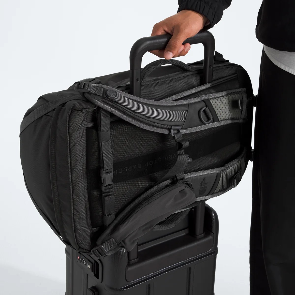 Black backpack with padded straps attached to the handle of a black rolling suitcase.