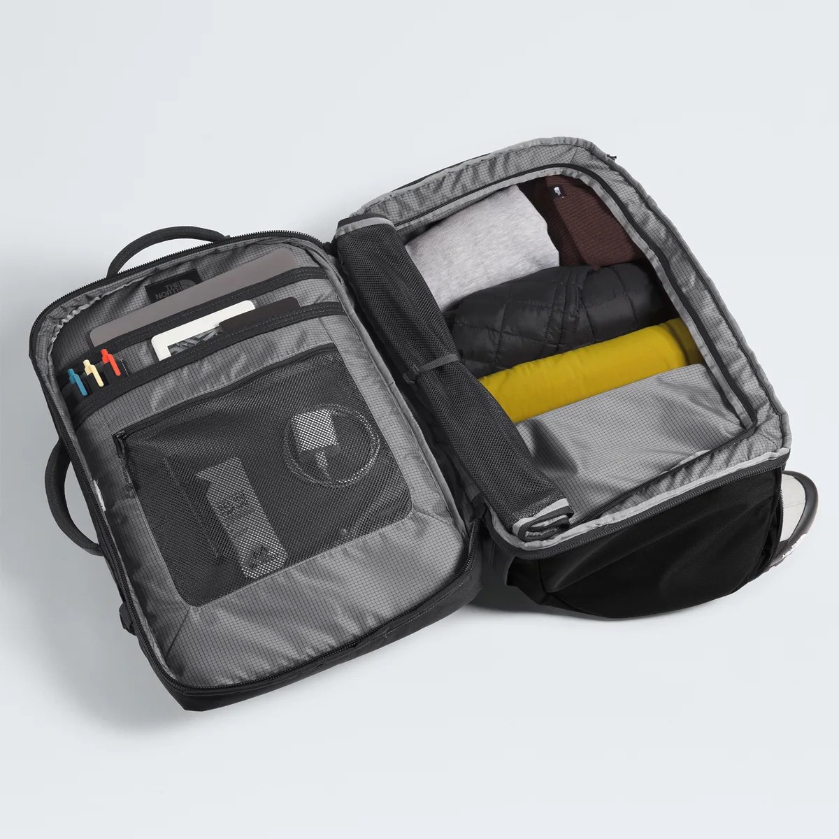 Open black and gray travel backpack with organized compartments holding folded clothes and accessories.