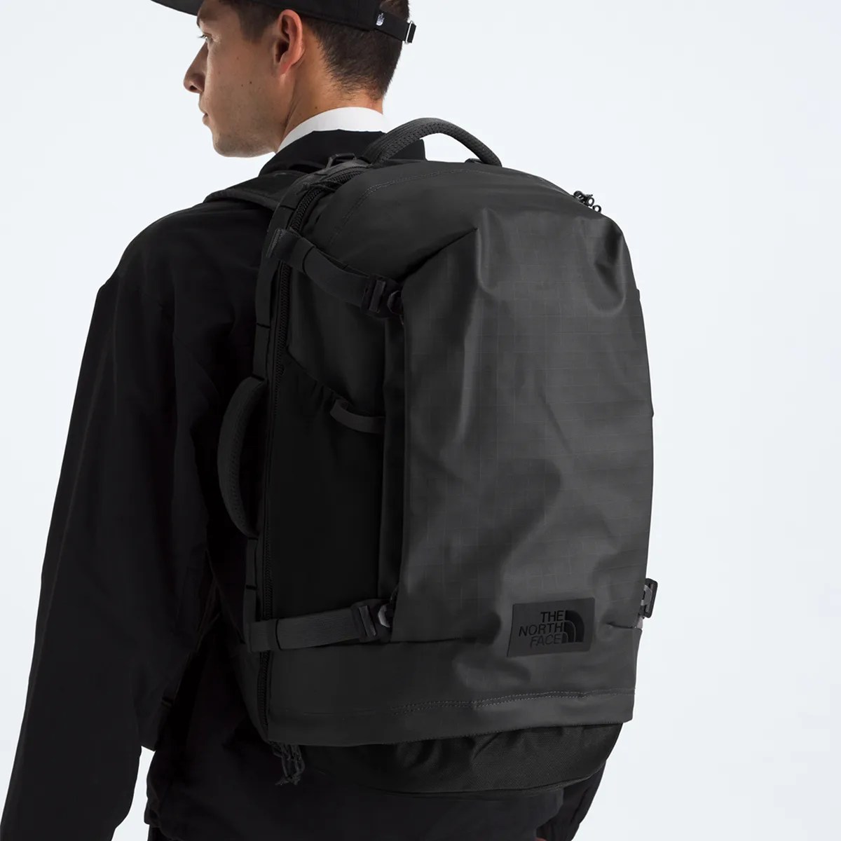Black rectangular The North Face backpack with side compression straps worn by a person in black clothing.