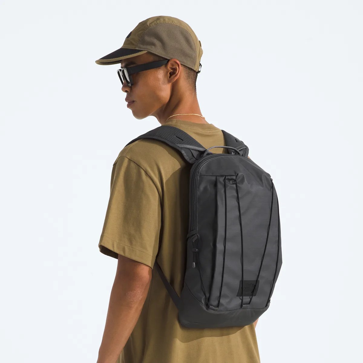 Black rectangular backpack with vertical straps worn by a person in a brown shirt and cap.