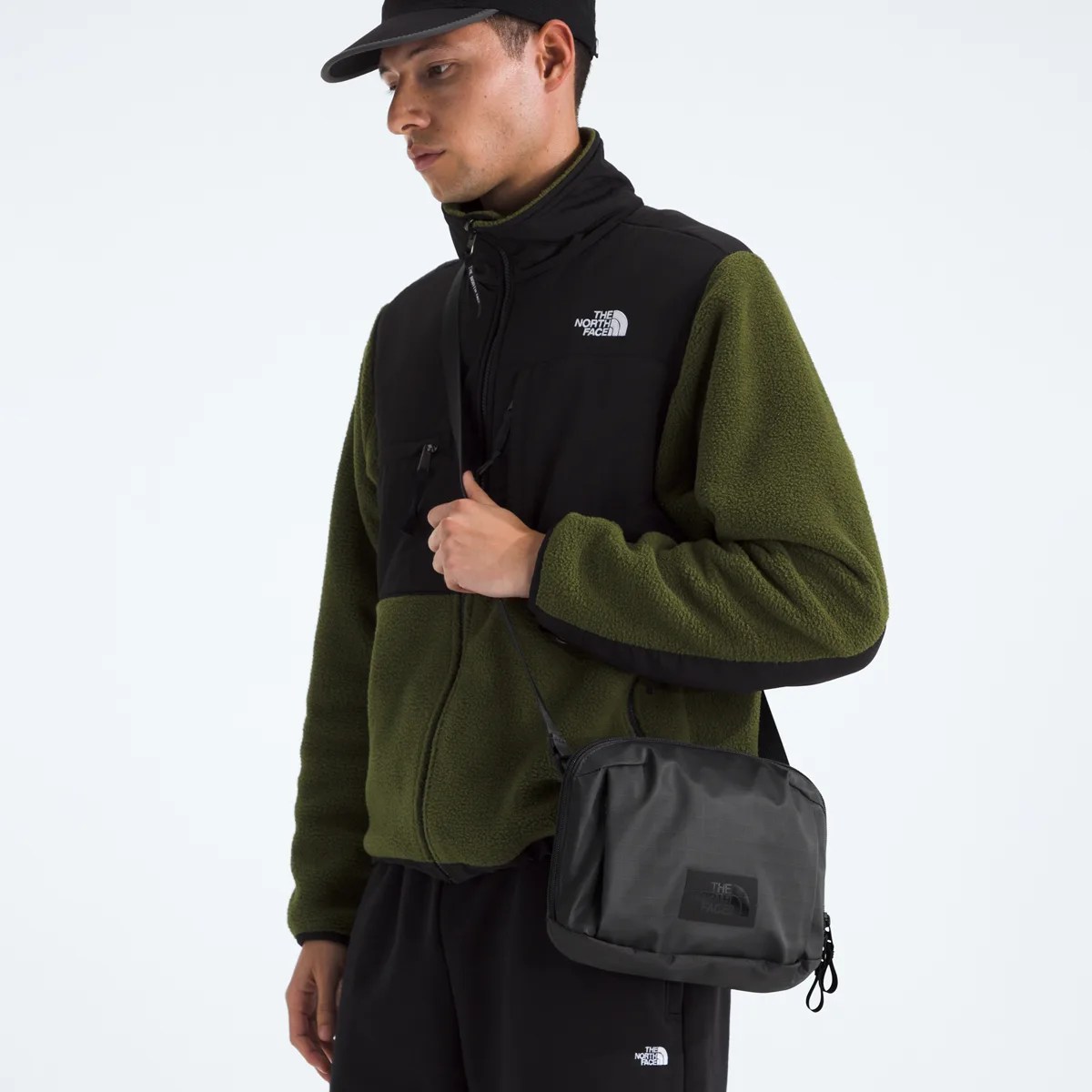 Black and olive green fleece jacket with The North Face logo worn by a person carrying a black crossbody bag.