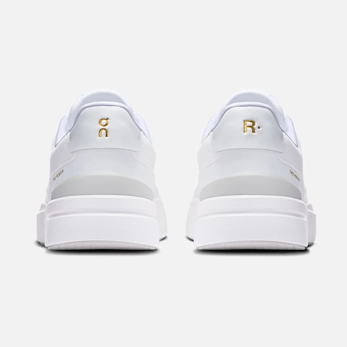 Pair of white sneakers with thick soles, gold logos on the heel tabs, and "THE ROGER" text on the sides.