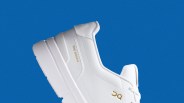 White sneaker with gold "THE ROGER" and "OC" logos on the side against a blue background.