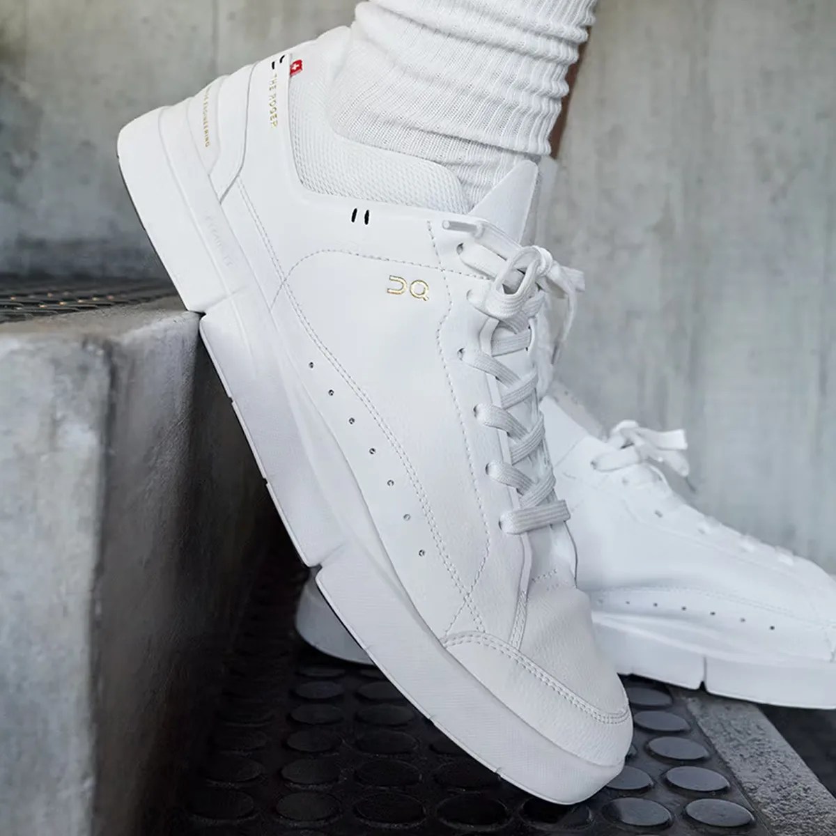 White leather sneakers with gold "DQ" logo and white laces worn with white ribbed socks.