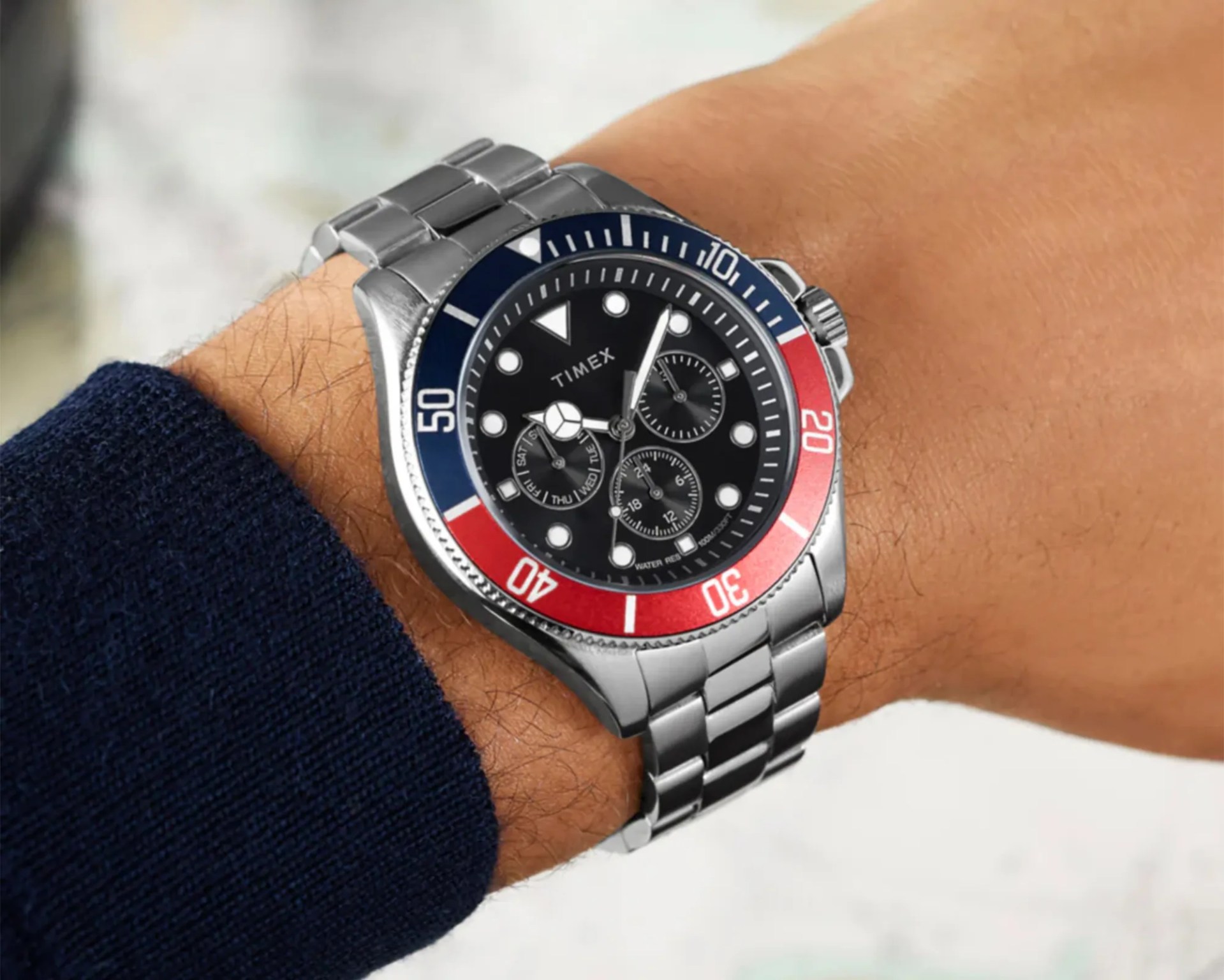 Silver Timex wristwatch with a black dial and red and blue bezel worn on a wrist.
