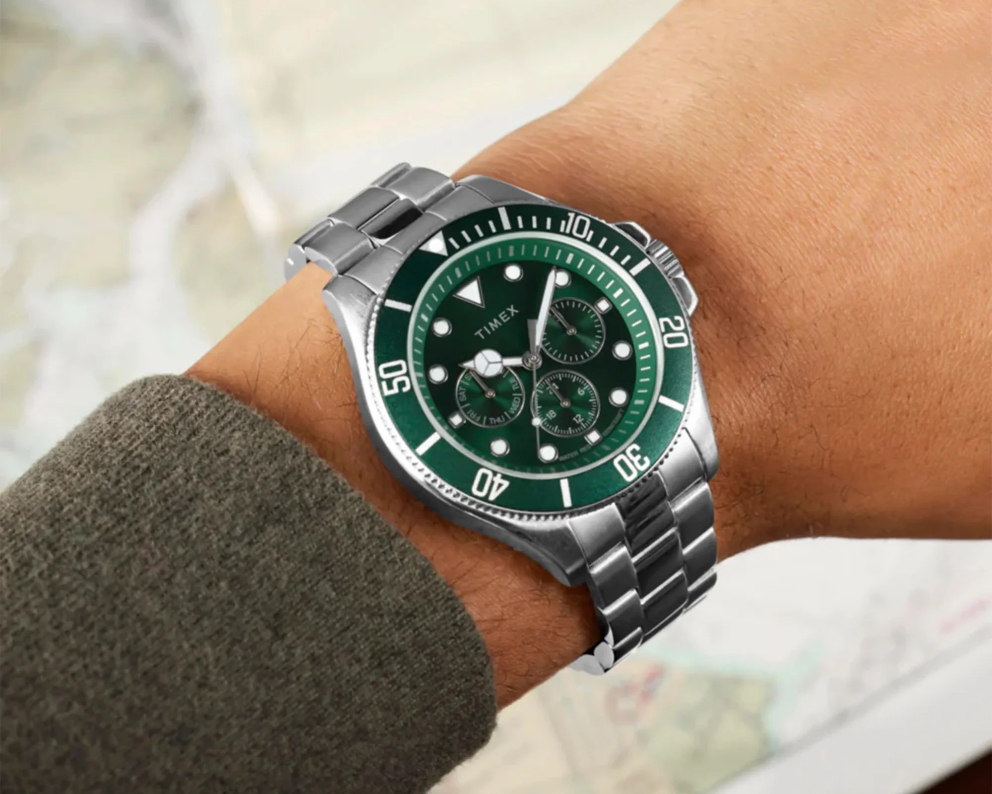 Silver metal Timex wristwatch with green dial and bezel worn on a wrist.