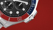 Close-up of a stainless steel watch with a black dial, red and blue bezel, and chronograph subdials.