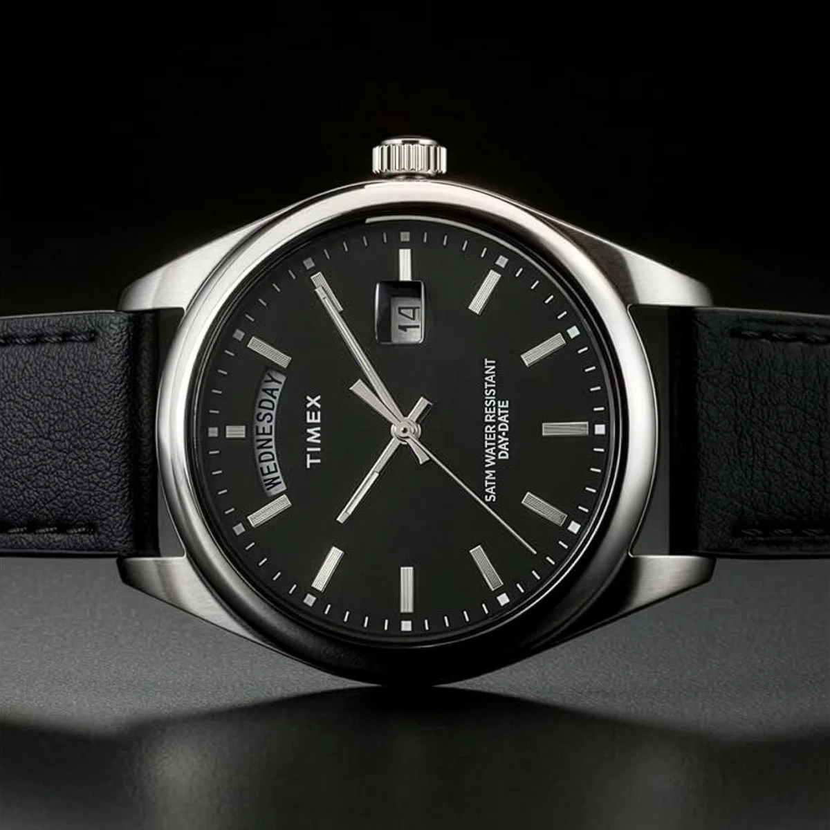 Black Timex wristwatch with silver markers, day-date display, and black leather strap on a dark surface.