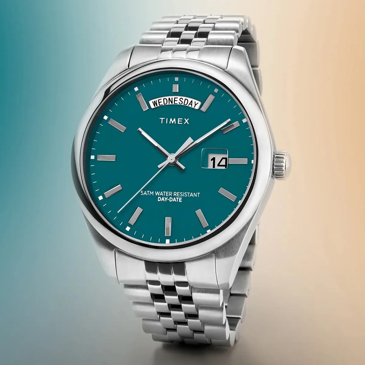 Silver stainless steel Timex wristwatch with teal dial, day-date display, and metal link bracelet.