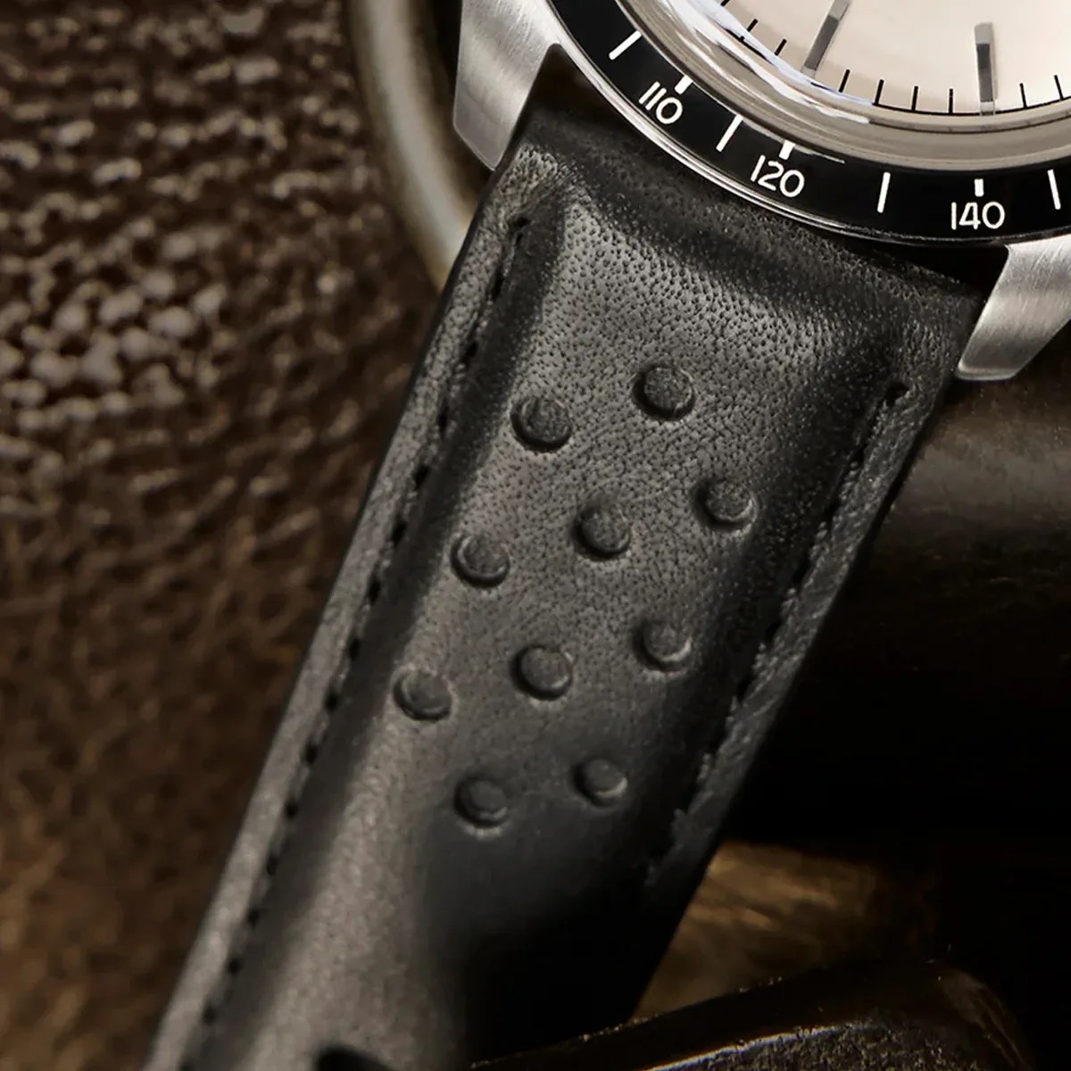 Close-up of a black perforated leather watch strap attached to a stainless steel watch case.